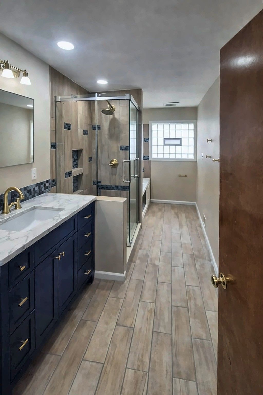 Remodeled bathroom with navy vanity, gold fixtures and glass shower